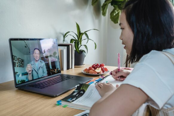 asian female student taking notes from her high school online teacher