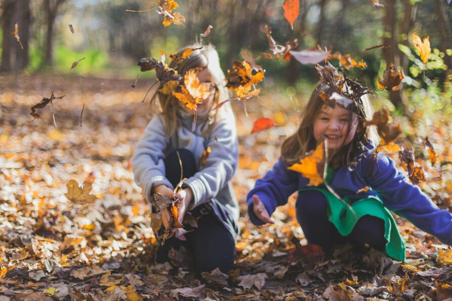 two elementary students playing with leaves in the park
