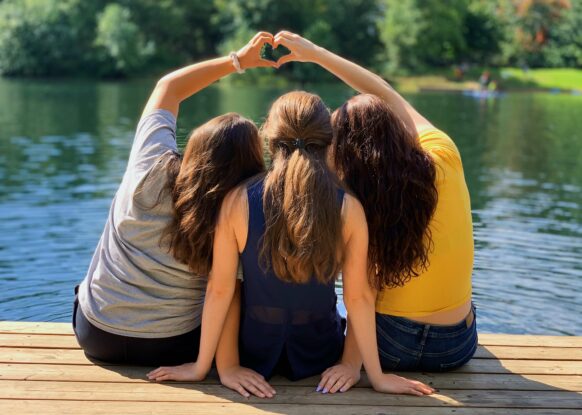 three girls on a dock making hearts with their hands