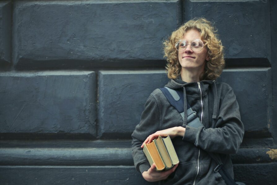 caucasian male student wearing a jacket and holding books 