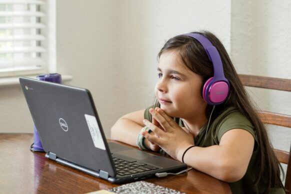 a young female student wearing headphones paying attention to her teacher on the laptop