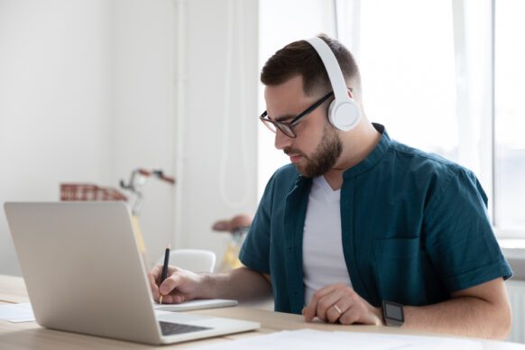 male student wearing a teal shirt and headphones doing homework on the computer